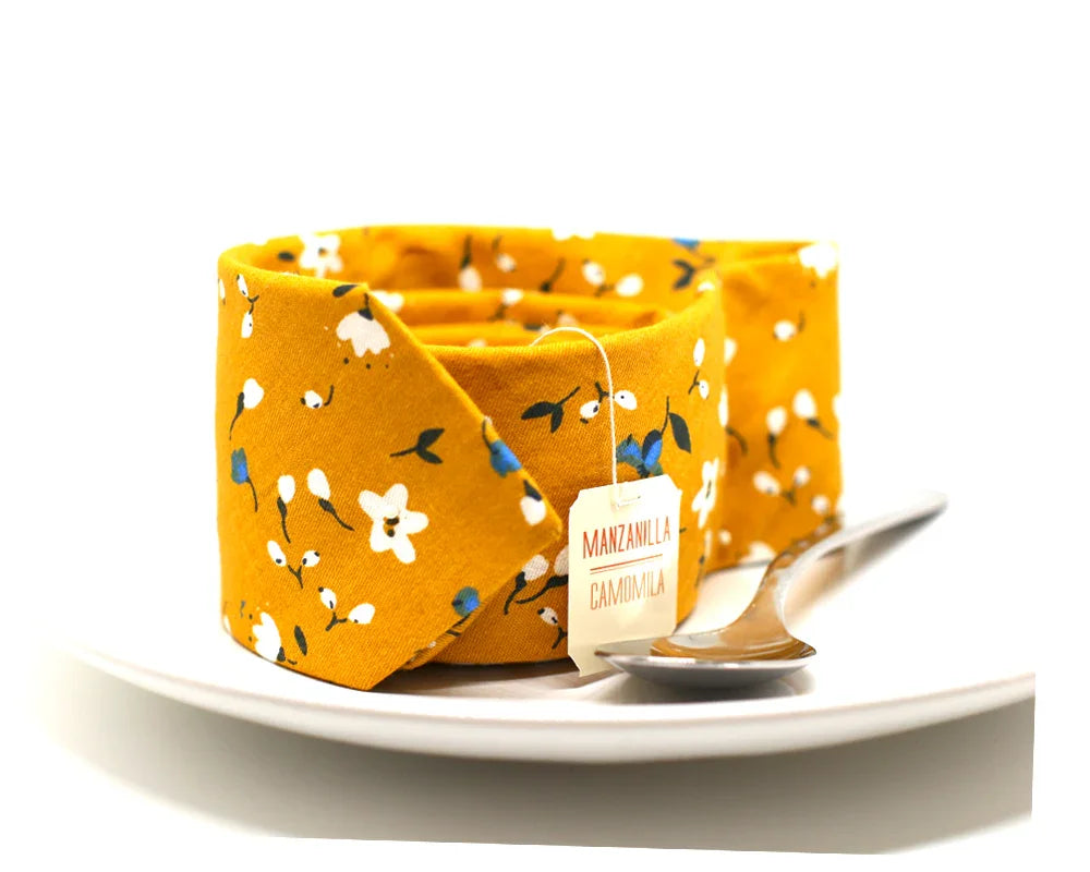 Pajarita mostaza con estampado floral sobre plato blanco con etiqueta manzanilla camomila y cuchara