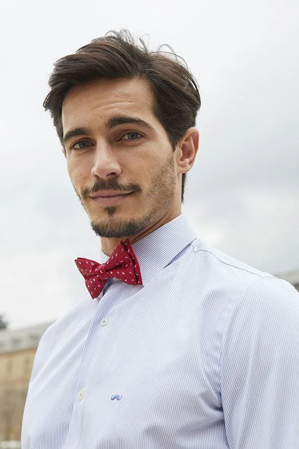 Hombre con pajarita roja estampada y camisa azul clara de rayas finas, estilo original y elegante