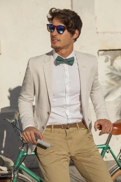 Hombre con pajarita verde, chaqueta clara y gafas de sol azules posando junto a bicicleta verde