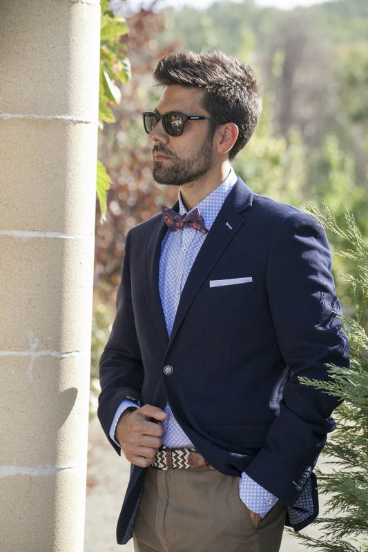 Hombre con pajarita estampada roja, chaqueta azul y gafas de sol, estilo elegante y original