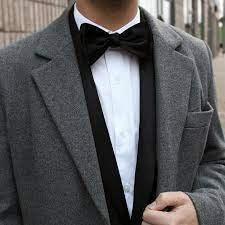Hombre vestido con pajarita negra, camisa blanca y chaqueta gris elegante en exterior urbano