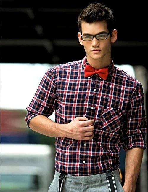 Hombre joven con camisa de cuadros y pajarita roja posando con gafas de marco negro, estilo original y moderno