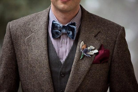 Hombre con pajarita azul de terciopelo y traje marrón con chaleco y flores en la solapa, estilo elegante y original