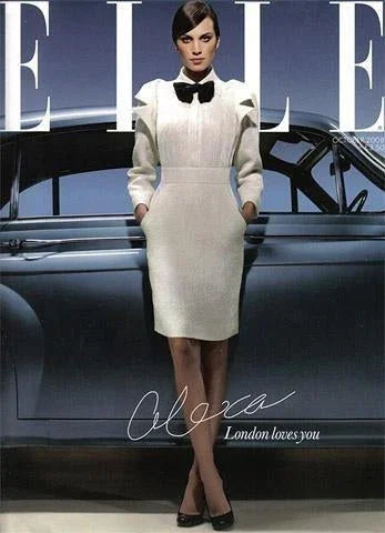 Mujer elegante con vestido blanco y pajarita negra posando frente a un coche retro, estilo sofisticado