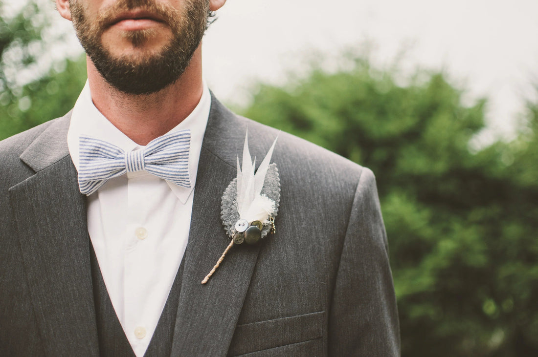 Hombre con traje gris, camisa blanca y pajarita a rayas blancas y azules detalle elegante para boda