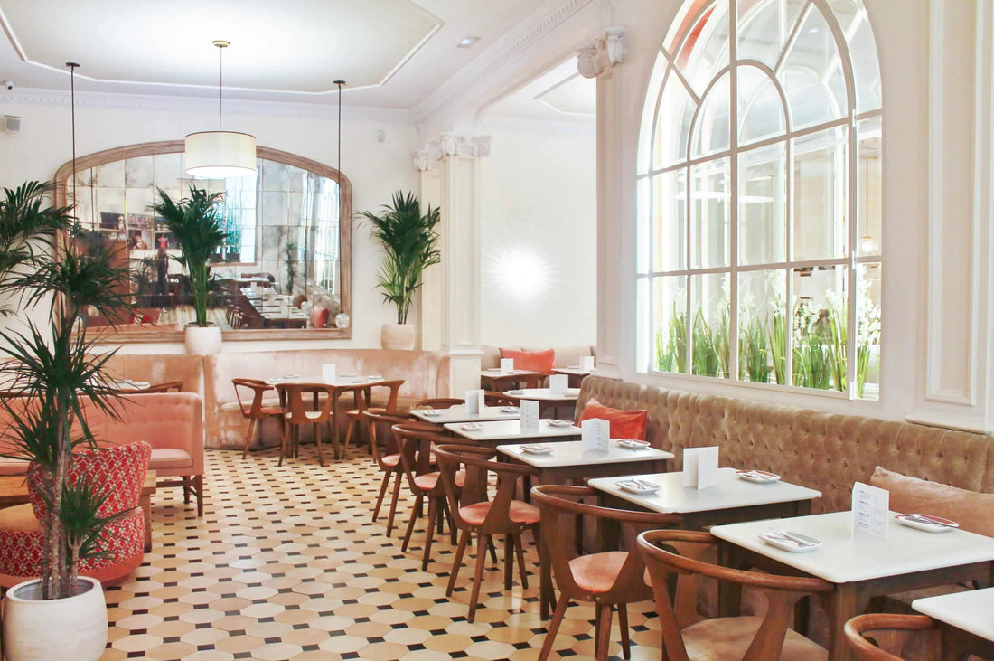 Interior luminoso y elegante de restaurante con sillas de madera, mesas blancas, sofás beige y plantas decorativas