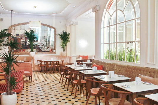 Interior luminoso y elegante de restaurante con sillas de madera, mesas blancas, sofás beige y plantas decorativas