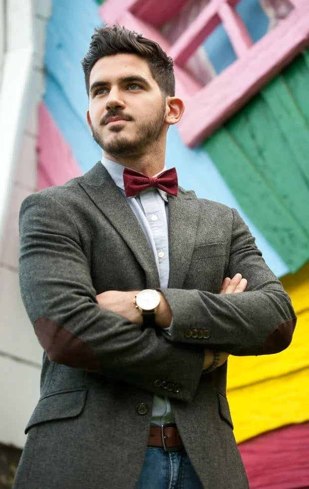 Hombre con pajarita roja y blazer gris posando frente a muro colorido en exterior, estilo original y elegante