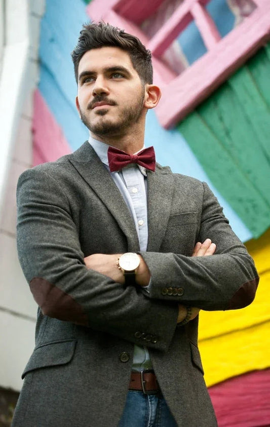 Hombre con pajarita roja y blazer gris posando frente a muro colorido en exterior, estilo original y elegante