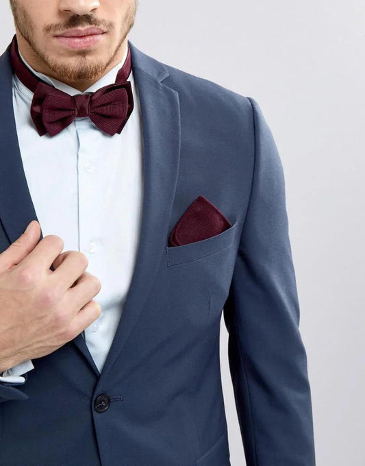 Hombre con traje azul, camisa blanca y pajarita burdeos a juego con un pañuelo de bolsillo